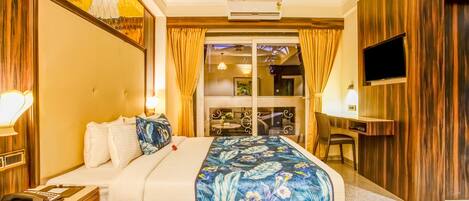 A hotel room with a bed, a desk, a television, and a balcony with curtains.
