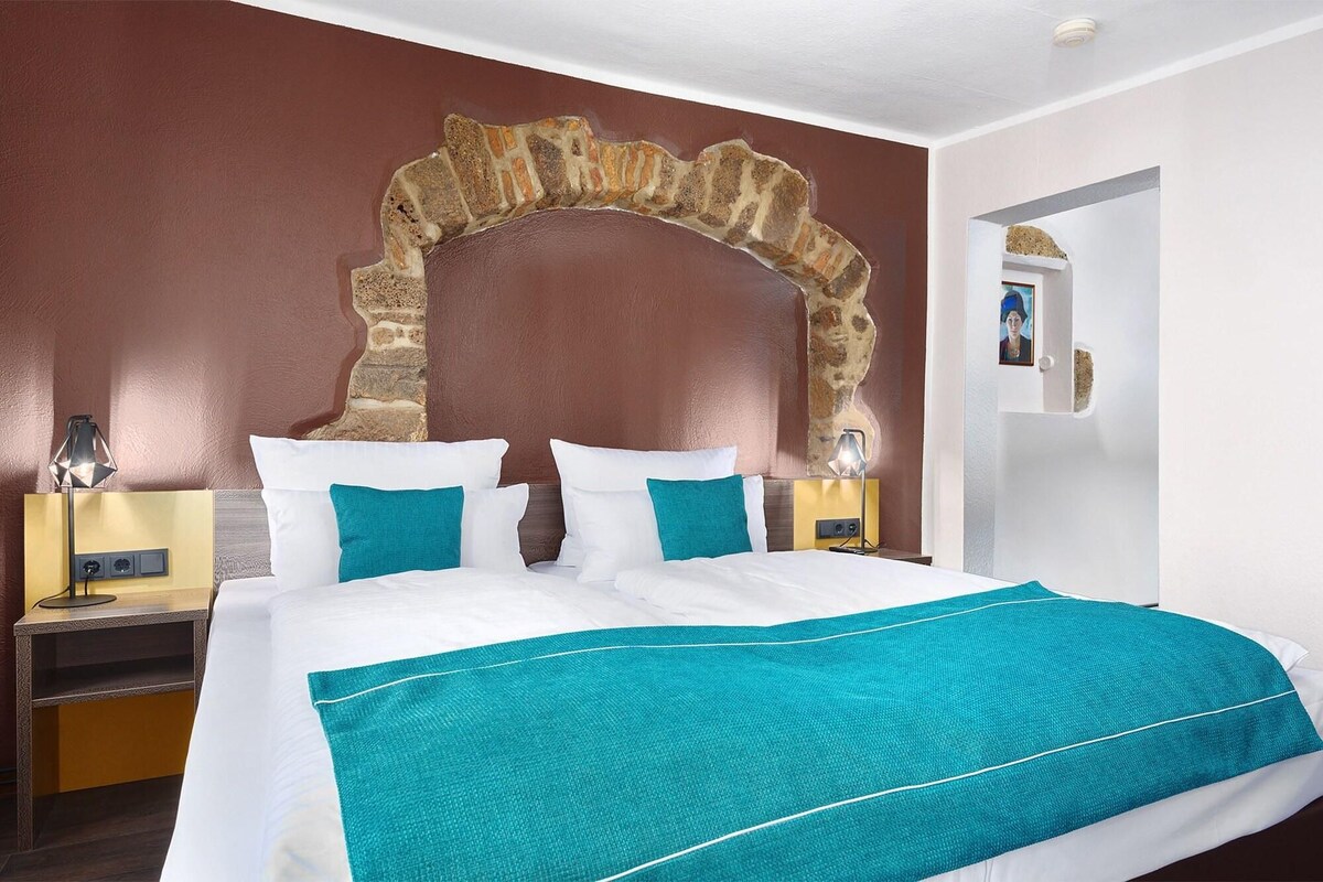 Habitación de hotel con una cama grande, un muro de arco de piedra y una puerta blanca.