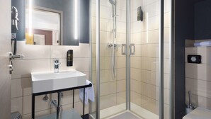 Un baño moderno con ducha envuelta en cristal, lavamanos blanco y espejo.