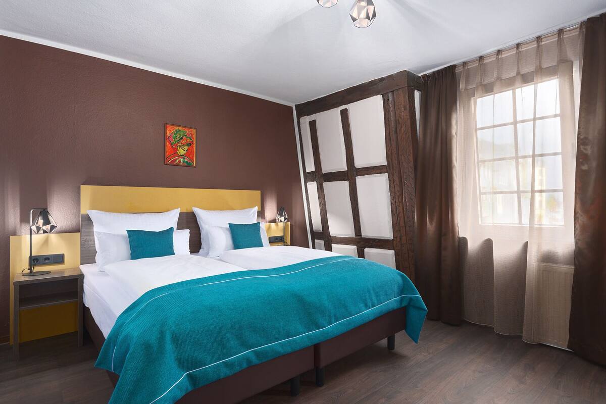 A neatly arranged bedroom with a large bed, a nightstand, a bedside table, and a window with curtains.