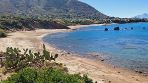Eine Küstenlandschaft mit einem Sandstrand, klarem blauen Wasser und Felsformationen.