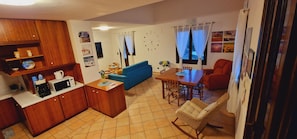 A compact living space with a kitchenette, a blue sofa, a dining table with chairs, and a wicker rocking chair.