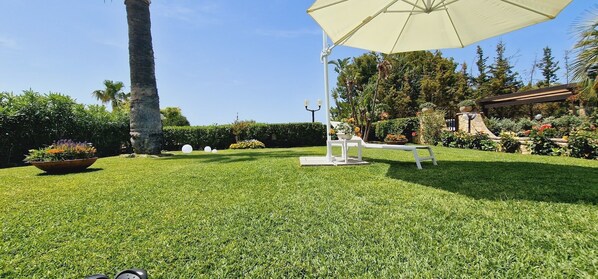 A well-maintained lawn with a white table and umbrella, surrounded by lush greenery and a variety of plants.