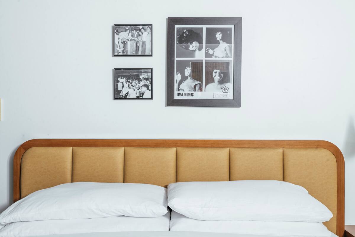A bedroom with a wooden headboard, white bedding, and two framed photographs on the wall.