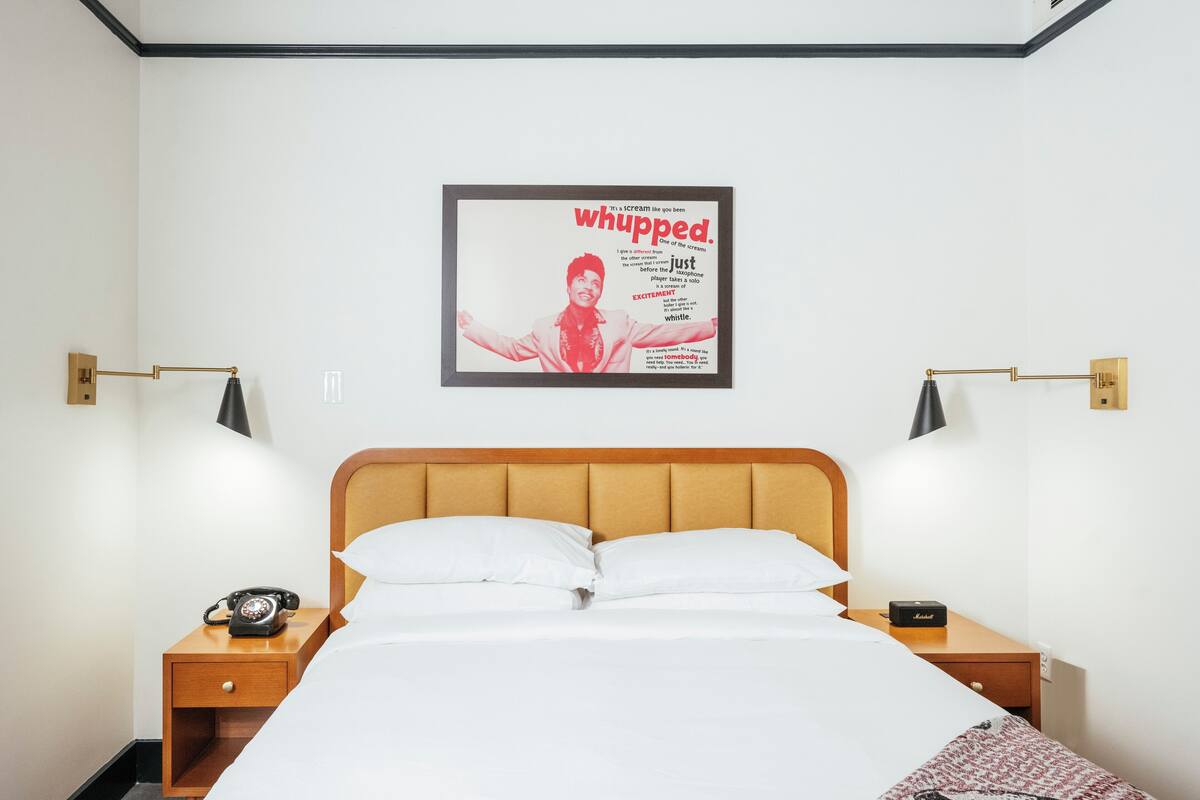 A hotel room with a bed, two bedside tables, a telephone, and a framed poster on the wall.