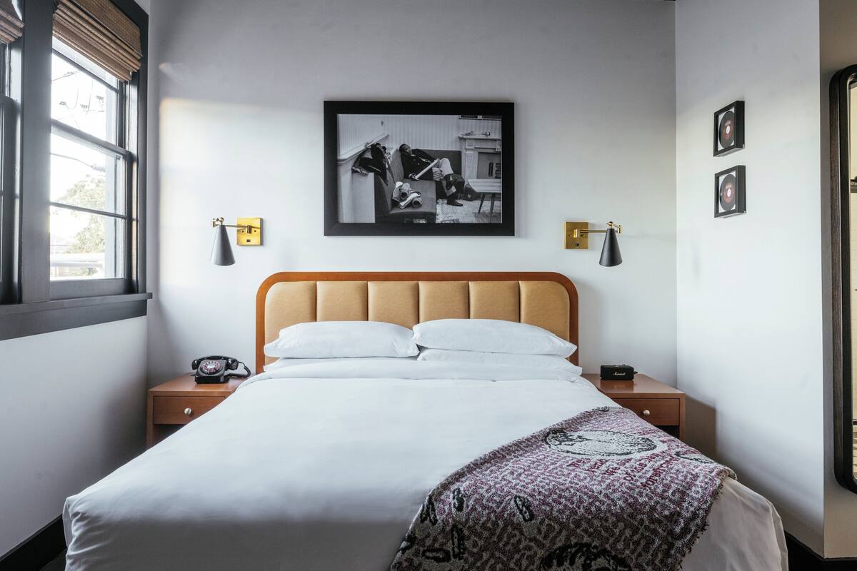 A neatly made bed with a patterned throw, a bedside telephone, and a framed black and white photograph on the wall.
