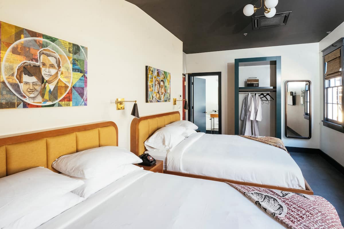 A hotel room with two beds, a large mirror, and artwork on the walls.