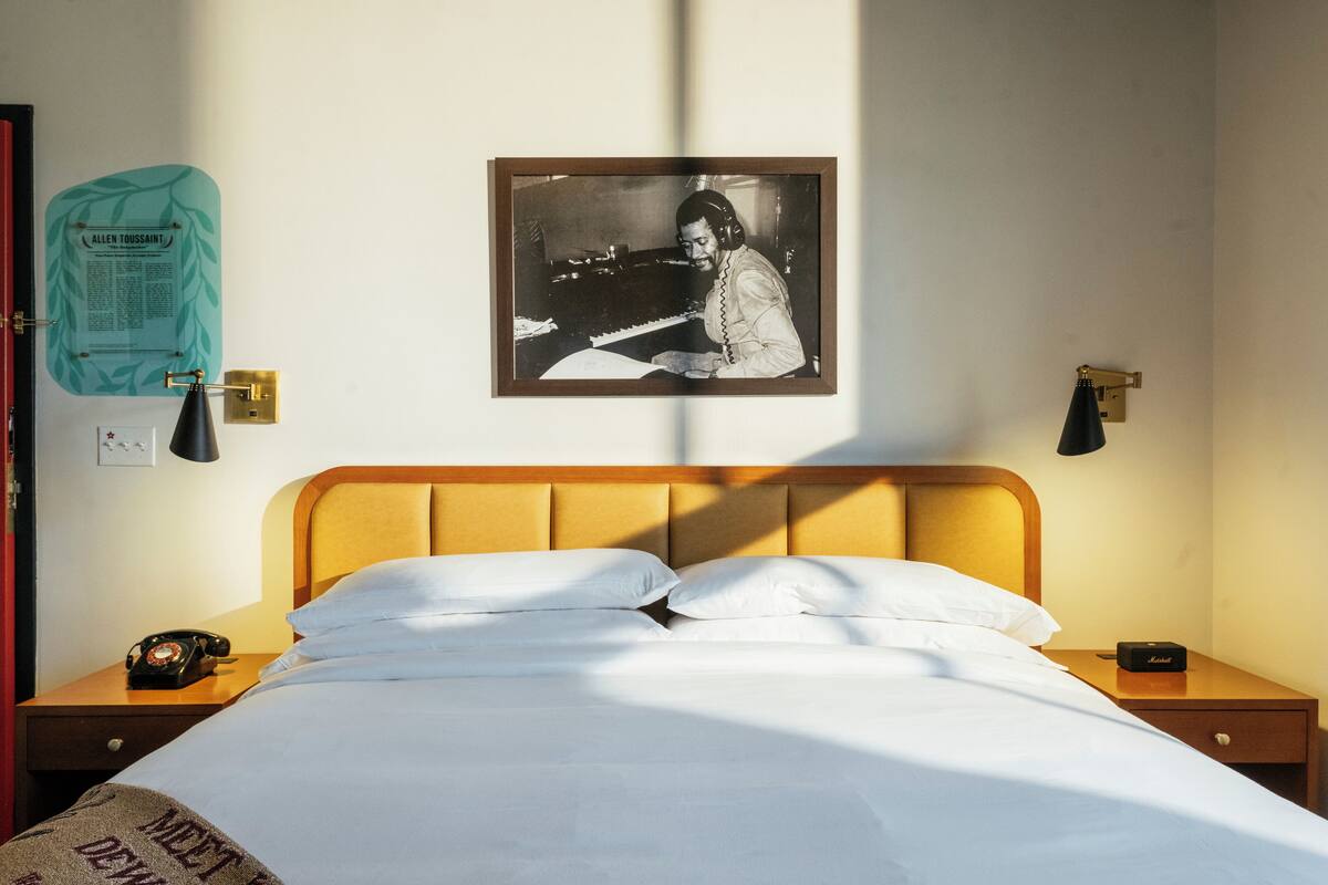 A hotel room with a bed, a nightstand, a telephone, a framed picture on the wall, and a light switch.