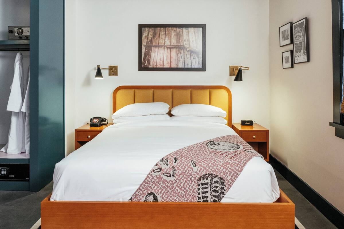A modern bedroom with a wooden bed, two bedside tables, a black and white rug, and a ceiling light fixture.