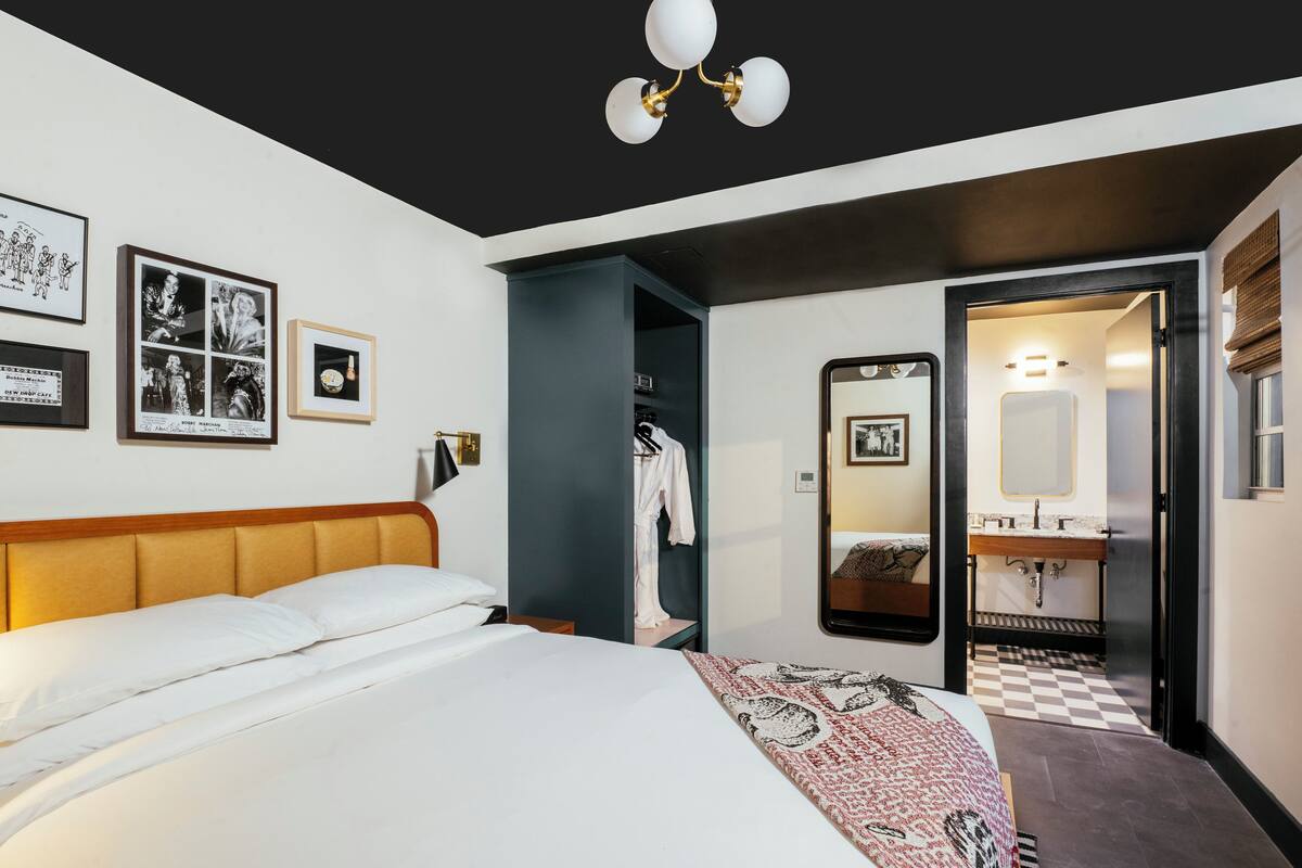 A hotel room with a bed, a wardrobe, a mirror, and a bathroom visible through an open door.