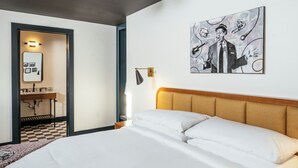 A hotel room with a large bed, a wooden headboard, a painting on the wall, and a desk with a mirror and lamp.