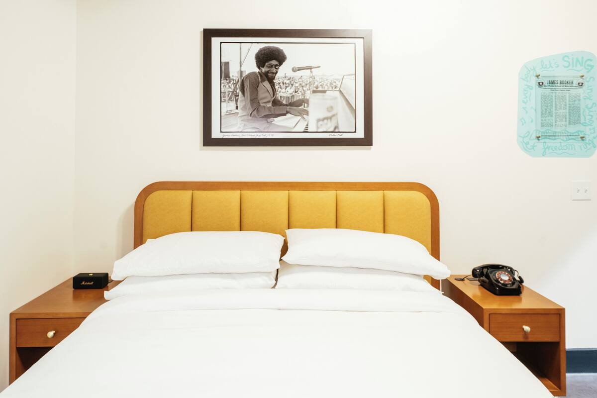 A neatly made bed with white linens, a wooden headboard, and a framed picture on the wall.