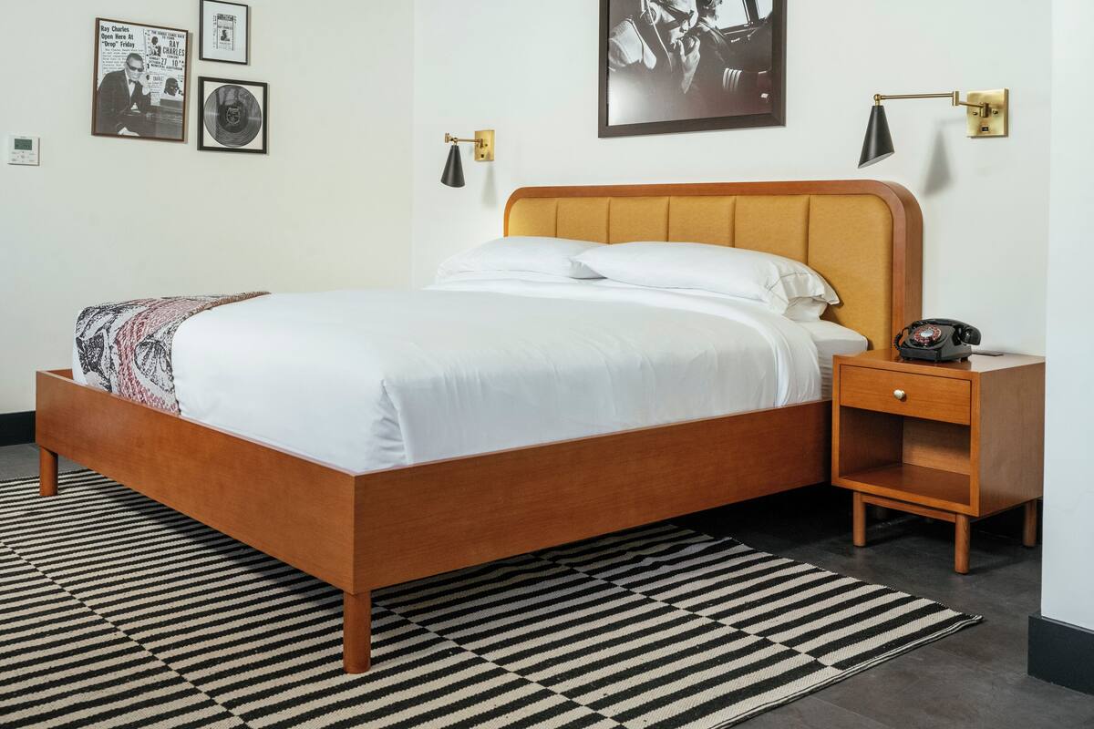 A neatly made bed with a wooden headboard, a bedside table with a lamp, and a framed picture on the wall.