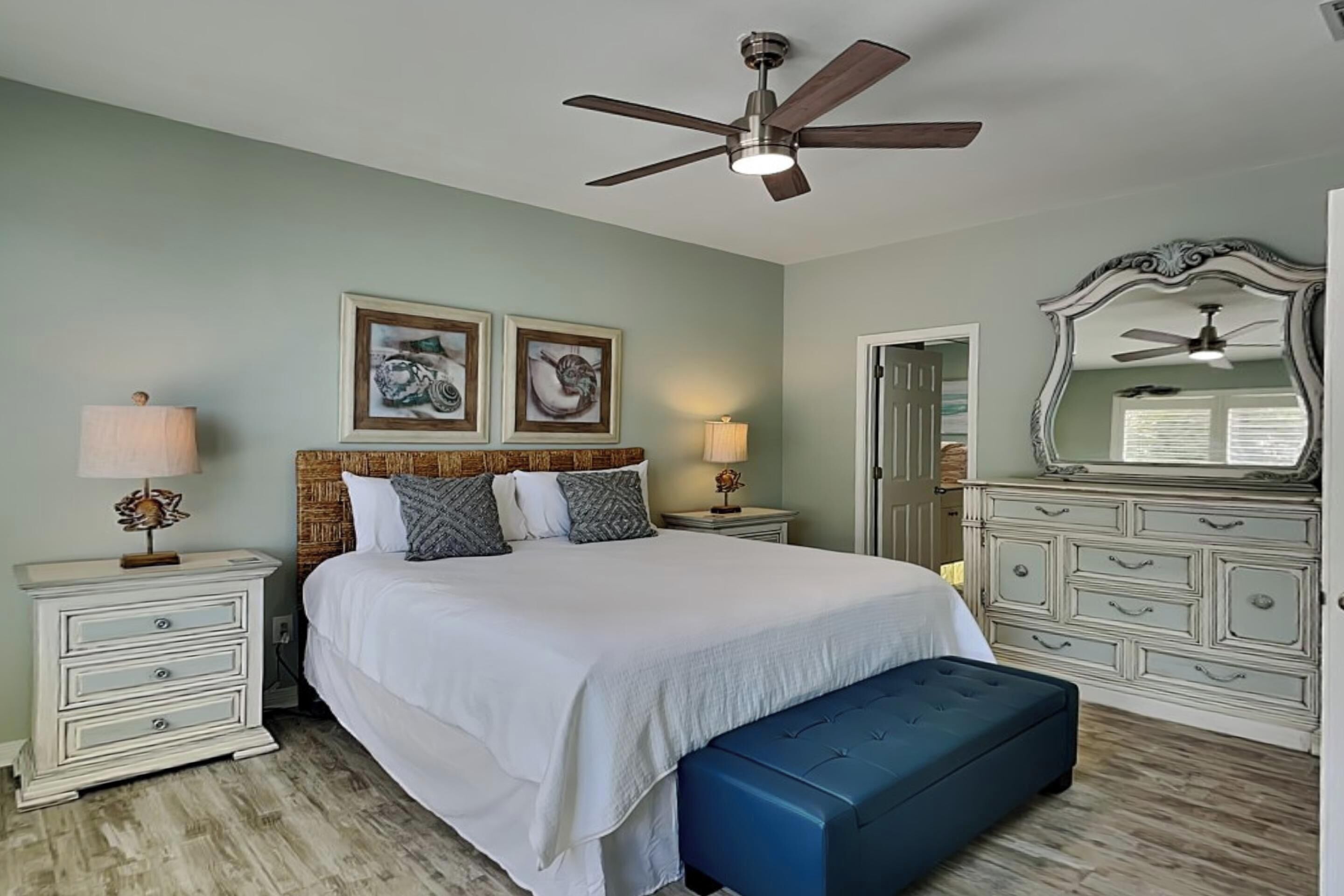 A bedroom with a bed, two bedside tables, a dresser, a mirror, and a ceiling fan.