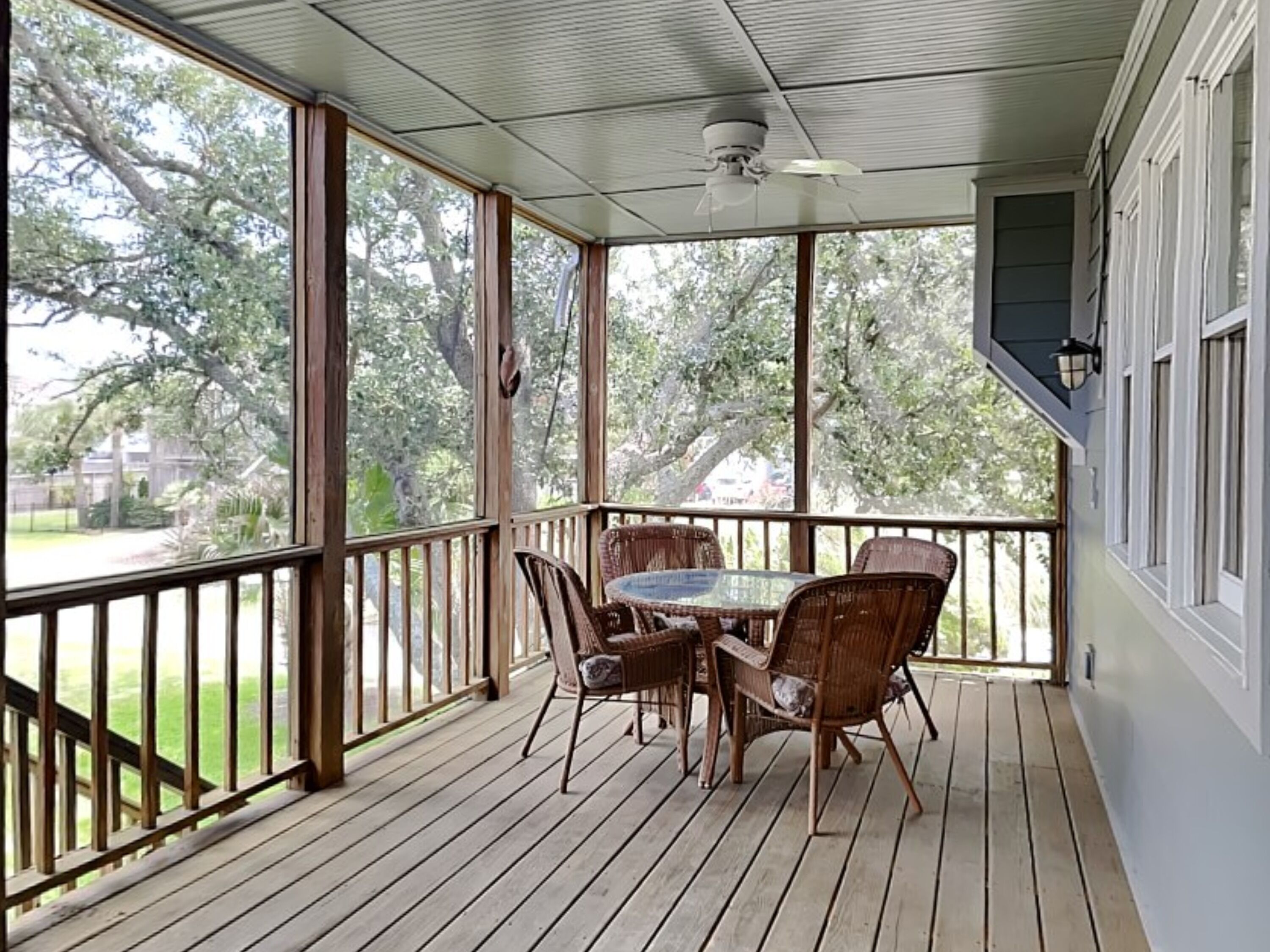 A covered porch with a table and chairs, large windows, and a ceiling fan.