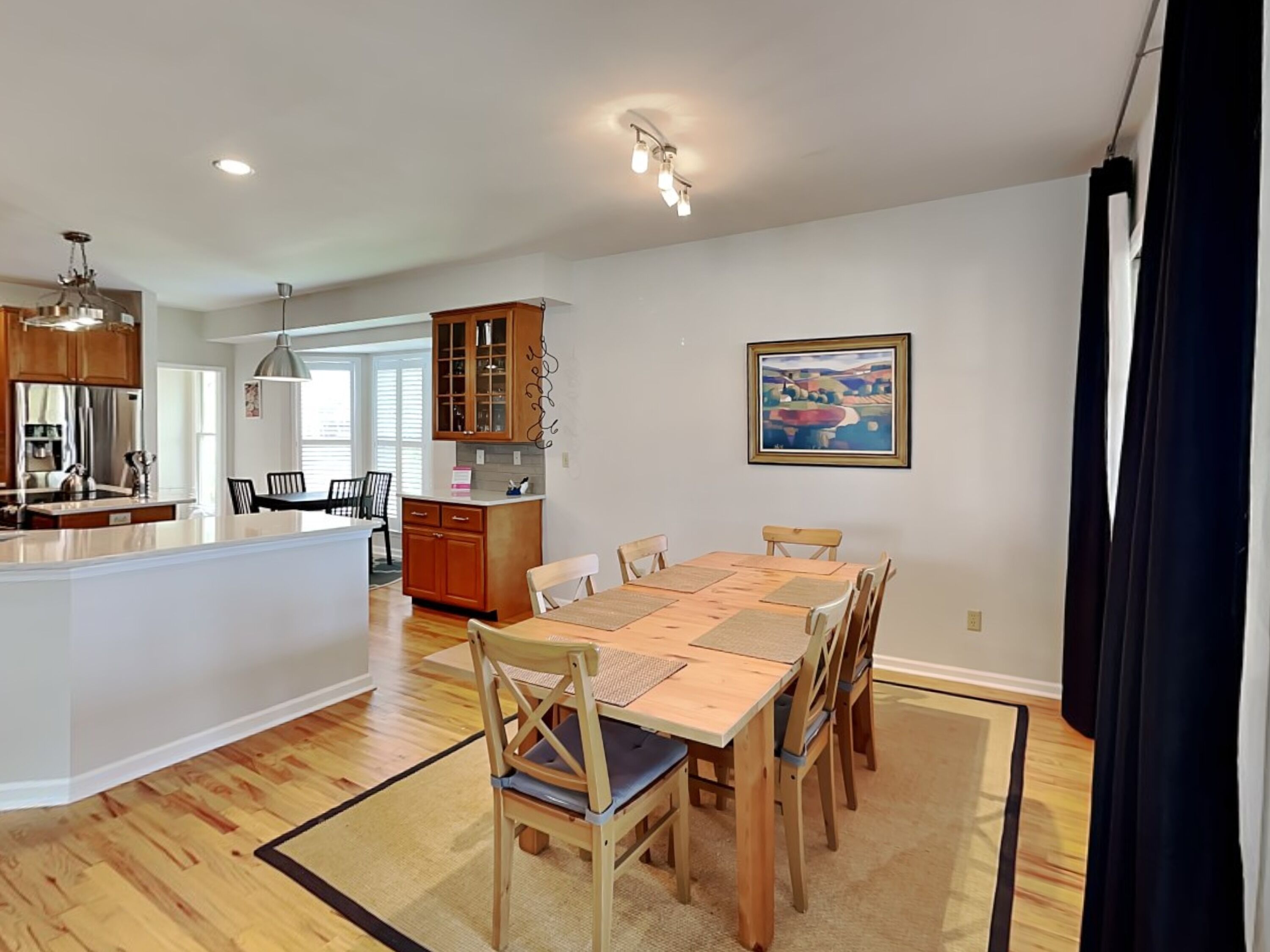 A spacious kitchen with wooden cabinets and a central island, a dining area with a large table and chairs, and a painting on the wall.
