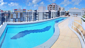 Piscina no terraço com borda azulejada, um caminho curvo e vista para edifícios ao redor.