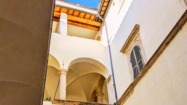 A narrow courtyard with arched doorways and a wooden balcony. - Elegance in Rome's Heart - Smart Lodging Prime (Roma)