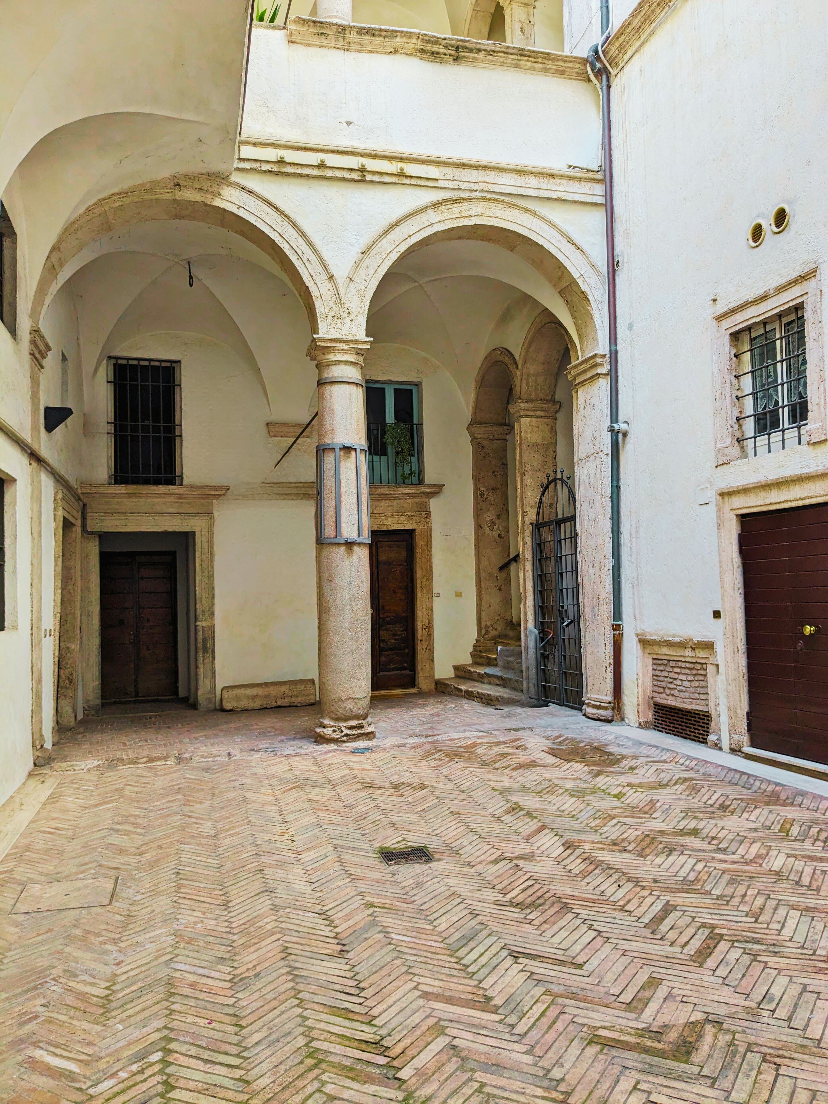 Un patio con suelo de diseño en espiga, arcos y una columna.