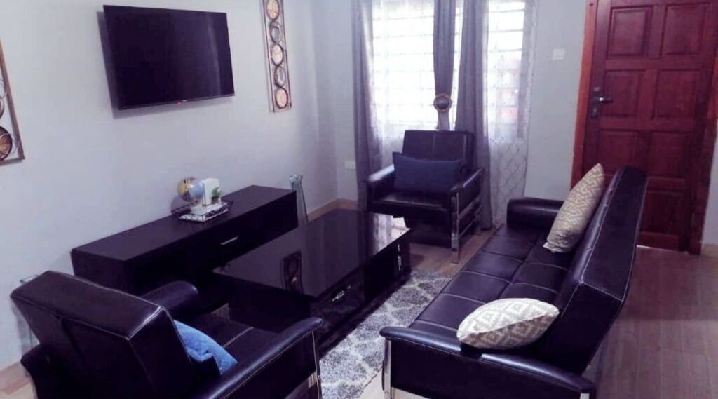 Een woonkamer met een zwarte bank, een zwarte fauteuil, een zwarte salontafel en een flatscreen televisie die aan de muur is bevestigd.