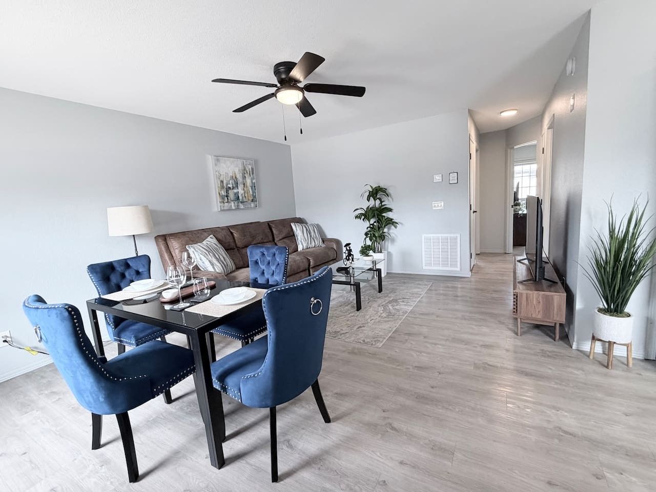 A modern dining area with a ceiling fan, a brown sofa with patterned cushions, and a dining table with blue upholstered chairs.