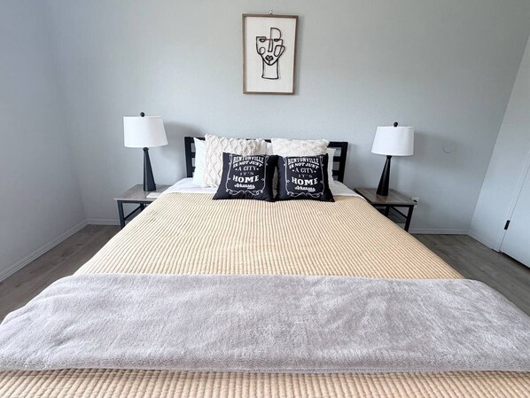 Un lit bien fait, recouvert d’une couverture à motifs, deux tables de chevet avec des lampes et une œuvre d’art encadrée accrochée au mur.