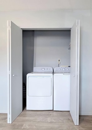 Une petite buanderie équipée de deux machines à laver à chargement frontal blanches et d’un sèche-linge, le tout dissimulé derrière une porte blanche.