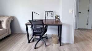 Quarto com escrivaninha de madeira, cadeira de escritório preta e relógio fixado na parede.