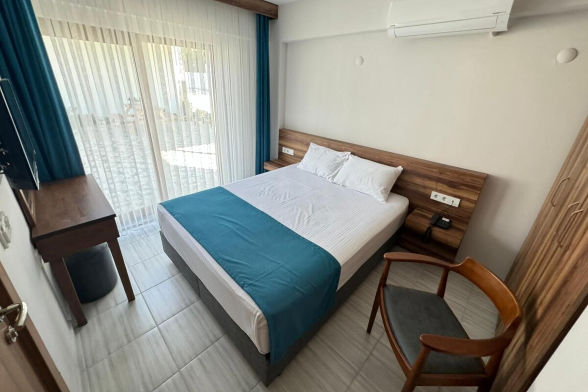 A hotel room with a bed, a desk, a chair, and an air conditioning unit.