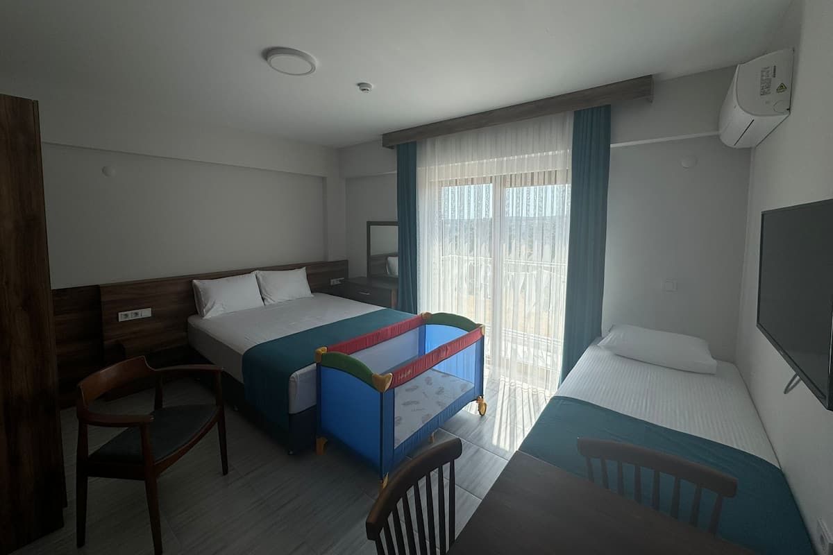 A hotel room with two single beds, a desk, a chair, a TV, and a window with curtains.