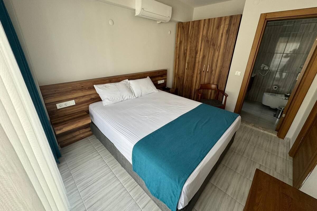 A neatly made bed with white and teal bedding, a wooden headboard, and a wooden wardrobe with a mirror.