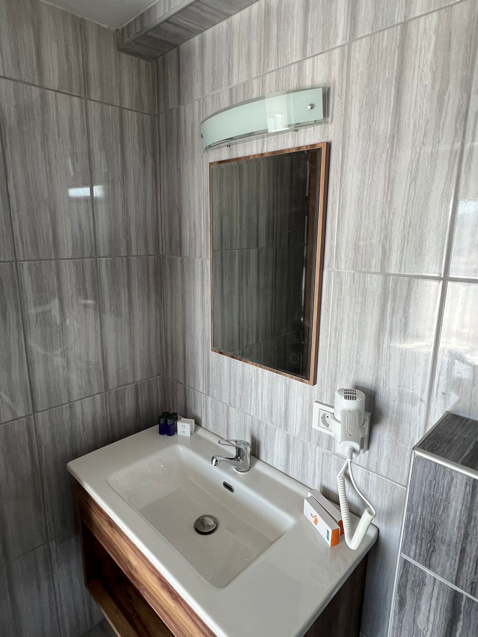 Un baño moderno con un lavamanos rectangular, un espejo y un secador de pelo montado en la pared.