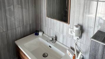 Un baño moderno con un lavamanos rectangular, un espejo y un secador de pelo montado en la pared.