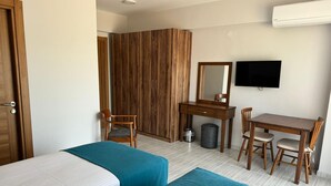 A hotel room with two beds, a desk, a chair, a wardrobe, a television, and a trash bin. - Troilus Park House Hotel (Eceabat)