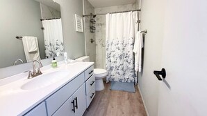 Een badkamer met een wit wastafelmeubel, toilet en douchegordijn.