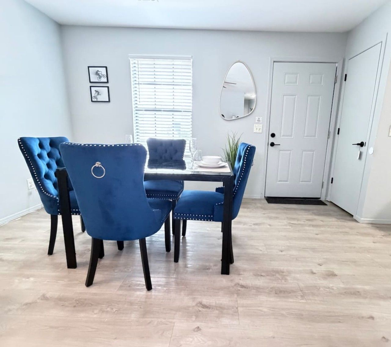 A dining area with a table and four blue upholstered chairs, a white door, and a window with blinds.