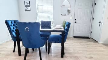 A dining area with a table and four blue upholstered chairs, a white door, and a window with blinds.
