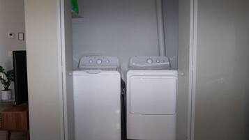 A laundry room with two white washing machines and a television on a stand.
