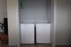 A laundry room with two white washing machines and a television on a stand.
