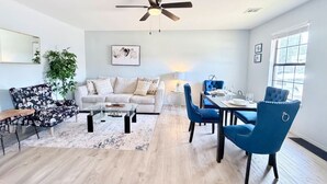 A modern living room with a sofa, coffee table, dining table, chairs, and a ceiling fan. - Townhome, Walk to The Momentary and Trails (Bentonville)
