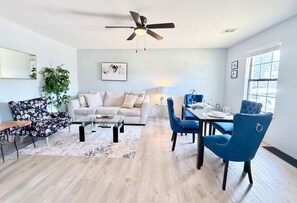 Uma sala de estar moderna com sofá, mesa de centro, mesa de jantar, cadeiras e ventilador de teto.