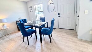 A dining area with a table and four chairs, a window with blinds, a door, and a wall-mounted mirror. - Townhome, Walk to The Momentary and Trails (Bentonville)