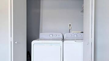 A compact laundry room with two white front-loading washing machines and a dryer, enclosed by a white door.