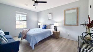 Quarto com cama, mesa de cabeceira, cadeira, janela e ventilador de teto.