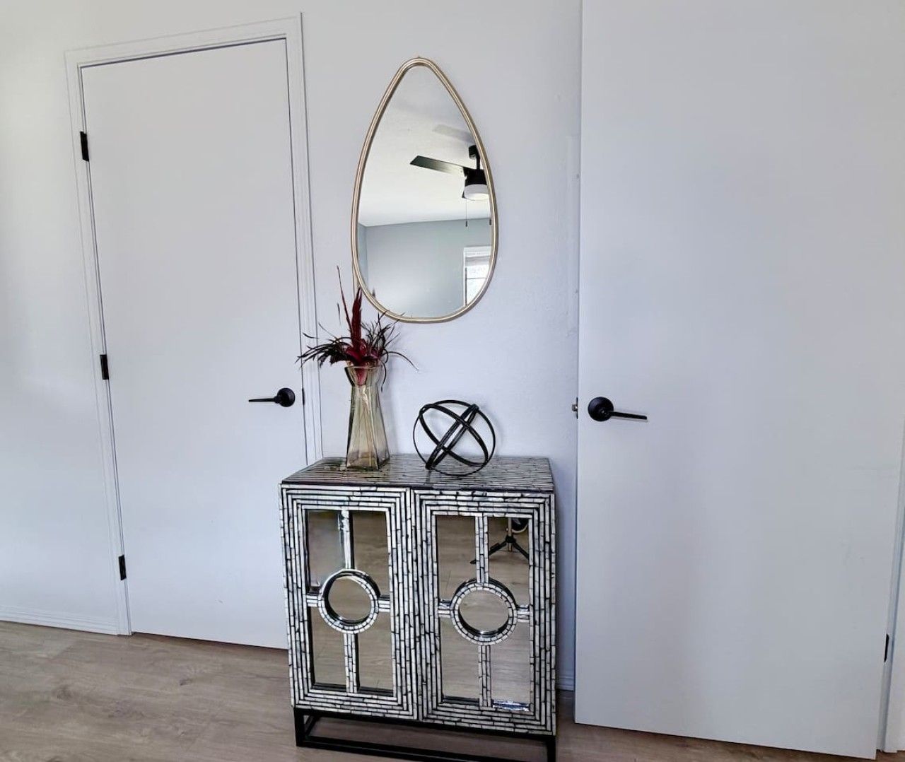 A white door with a black handle, a mirrored cabinet with a vase and a decorative sphere, and a ceiling fan.