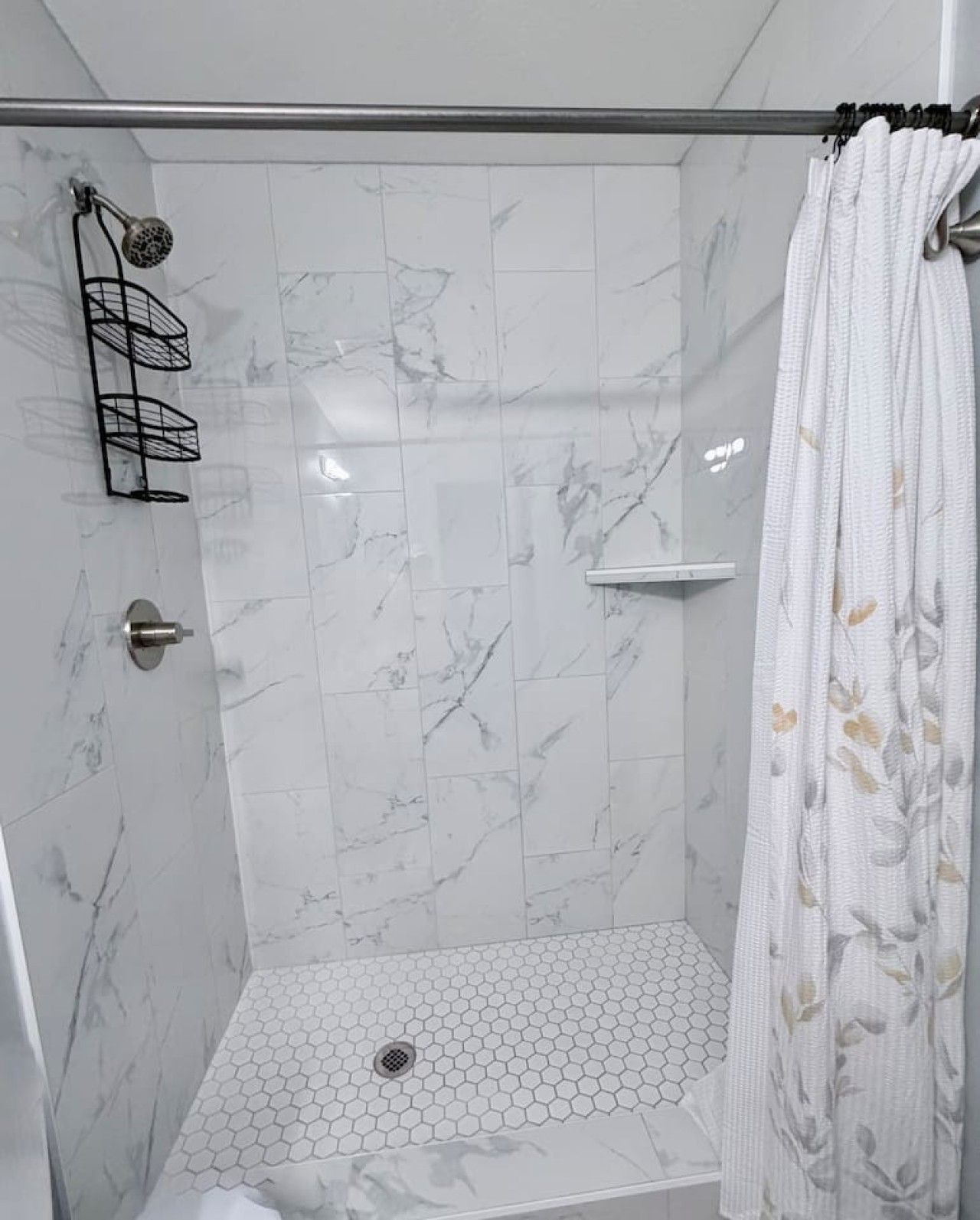 A shower with a glass door, marble tiles, a showerhead, a towel rack, and a shower curtain.