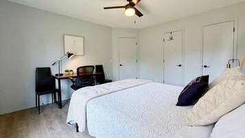 A bedroom with a bed, a desk, a chair, a ceiling fan, and two doors.
