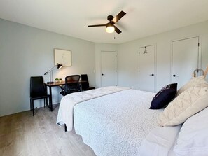 A bedroom with a bed, a desk, a chair, a ceiling fan, and two doors.