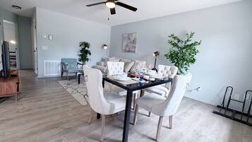 A modern dining area with a glass-top table, white upholstered chairs, and a ceiling fan.