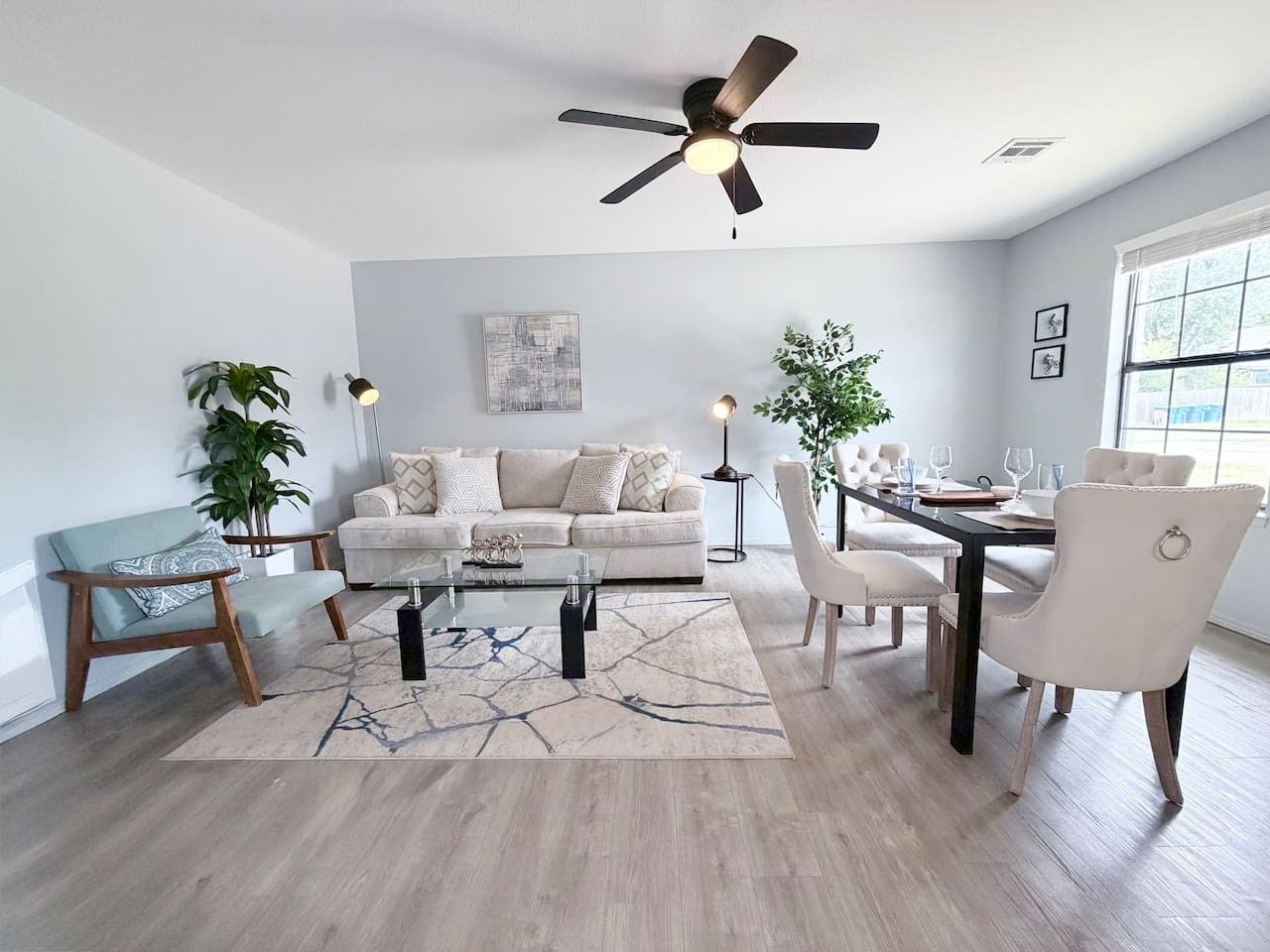 A modern living room with a sofa, coffee table, dining table, chairs, and a ceiling fan.